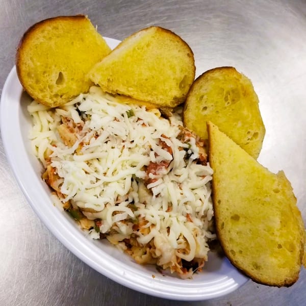 A white plate of cheesy pasta with four slices of golden garlic bread on a metal surface.