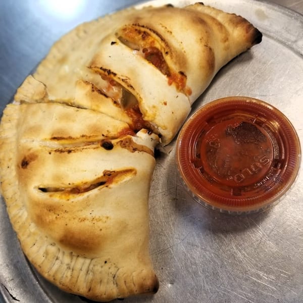 Two golden-brown calzones with visible cheese and sauce, served with a side of marinara on a metal tray.