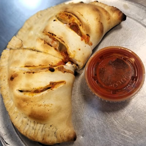 Two golden-brown calzones, sliced open to reveal melted cheese and sauce, with a side of marinara.