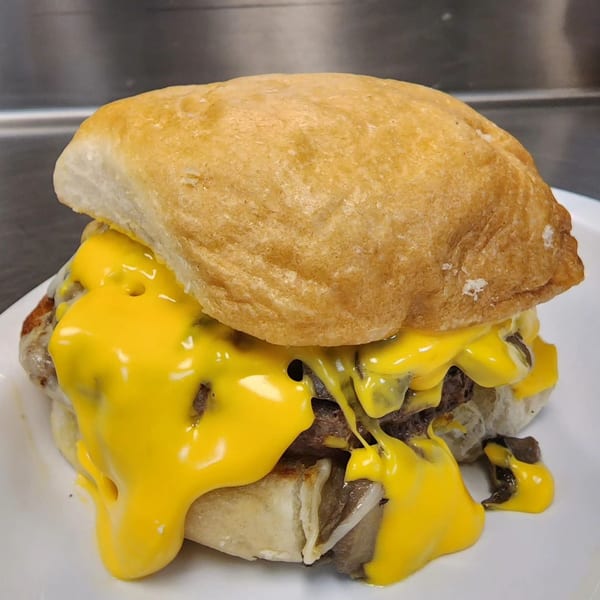 Cheesesteak sandwich with melted yellow cheese dripping down, served on a white plate.